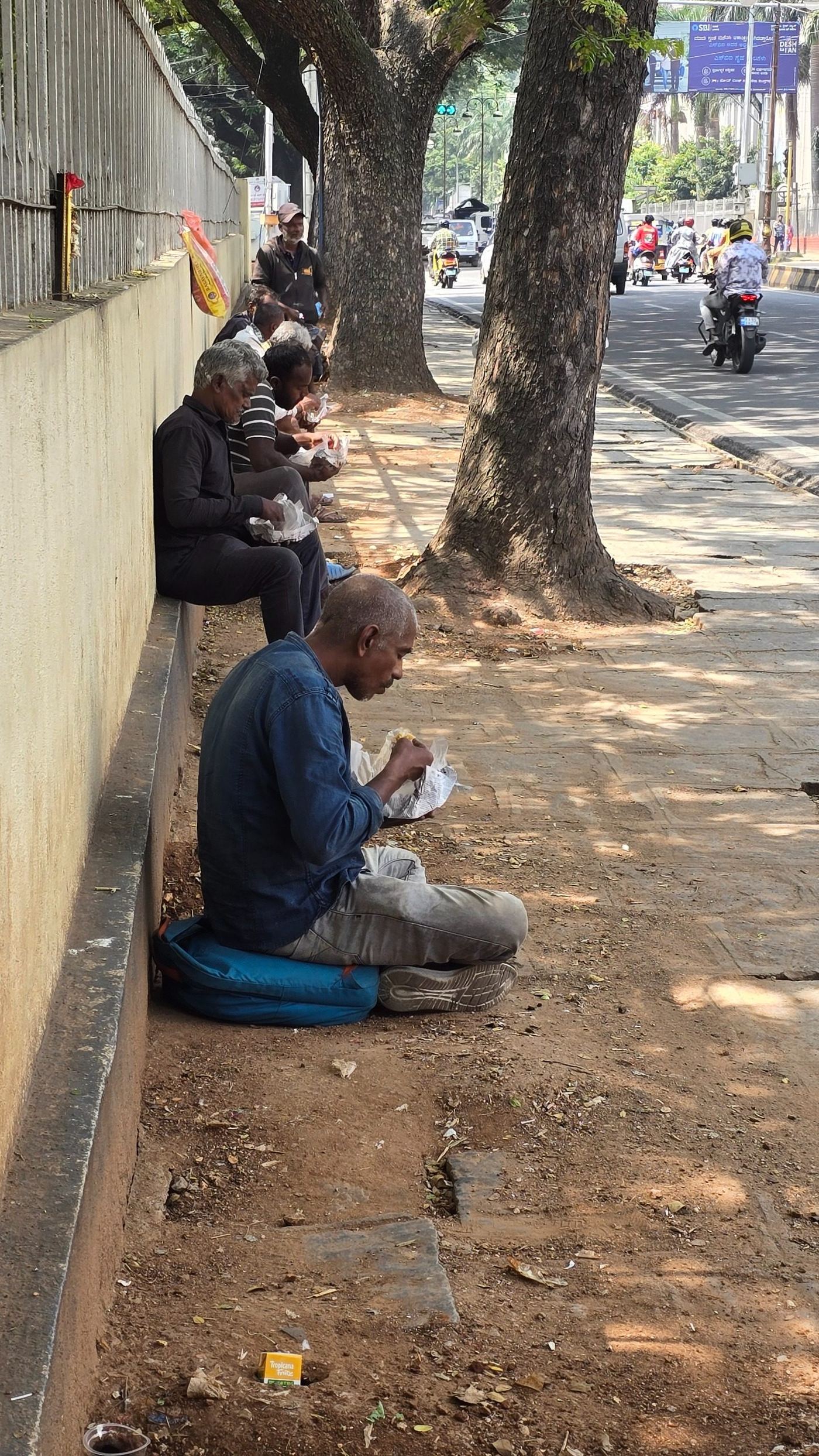 People eating food packets on a Mysuru footpath